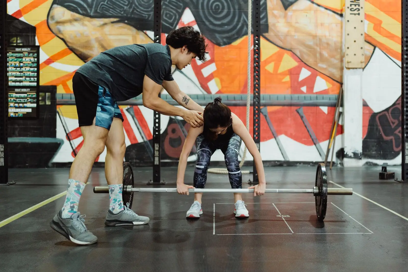 A coach talking a lifter through a set, standing beside the bar
